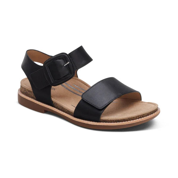 The Aetrex Women's Claire Black sandal by AETREX WORLDWide INC features a wide toe strap, ankle strap with a large black buckle, and a tan cushioned sole with slight heel—ideal arch-support sandals for all-day comfort.