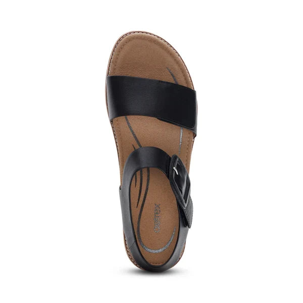 The Aetrex Women's Claire Black sandal by AETREX WORLDWide INC features a wide toe strap, a thinner buckled arch strap, and a tan cushioned insole with decorative stitching—ideal for stylish comfort.
