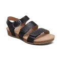 The Aetrex Women's Lilly Cutout Black sandal by AETREX WORLDWide INC features three adjustable perforated leather straps, a cork wedge sole, round silver buckle, tan cushioned insole with arch support, and floral design for all-day comfort.
