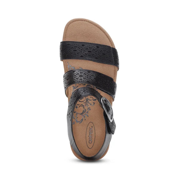 The Aetrex Women's Lilly Cutout Black sandal by AETREX WORLDWide INC features three perforated straps, a side buckle, and a tan cushioned insole with blue floral design. Enjoy built-in arch support for lasting comfort. Sandal is pictured from above.