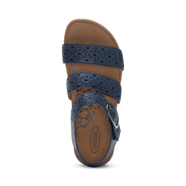 A top view of the Aetrex Women's Lilly Cutout Navy by AETREX WORLDWide INC shows three blue perforated straps with a buckle and a tan cushioned insole featuring a memory foam footbed, decorative details, and the AETREX logo on the heel.