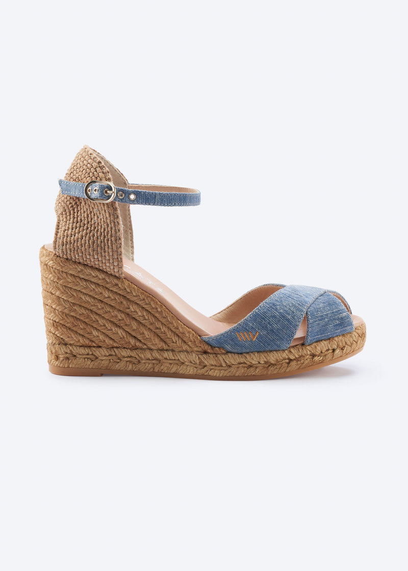 Side view of washed denim wedge espadrille sandal with ankle strap, crossover front straps, and a natural braided jute wedge, handcrafted in Spain