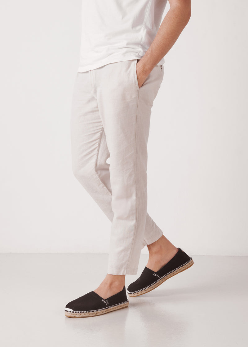 Male model walking in black canvas slip-on men’s espadrilles with braided jute sole, studio background.