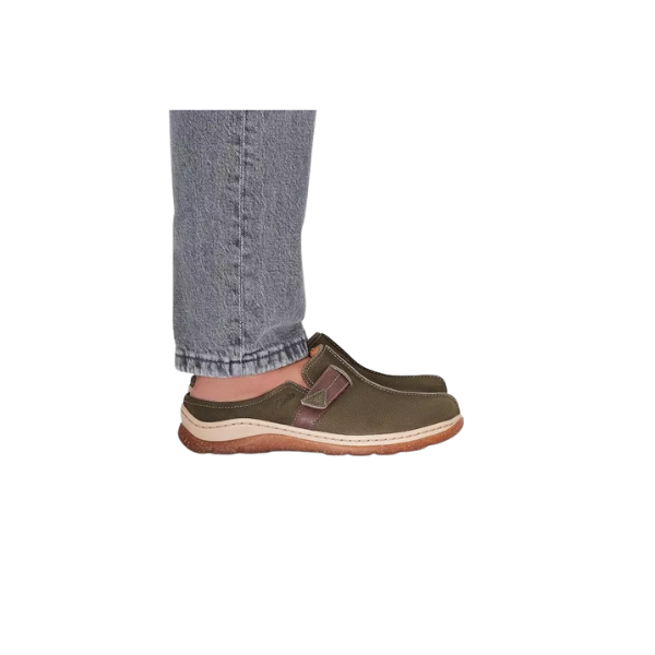 A person wearing gray jeans and CLARKS Orlene Clog Olive Combination Nubuck women's slip-on shoes with brown soles stands on a white background.