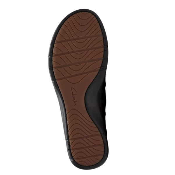 The image shows the sole of the CLARKS Women's Certina Joy Wide Brown boot, featuring black edges, a brown center with curved tread patterns, and the CLARKS brand name near the center—showcasing their quality craftsmanship.