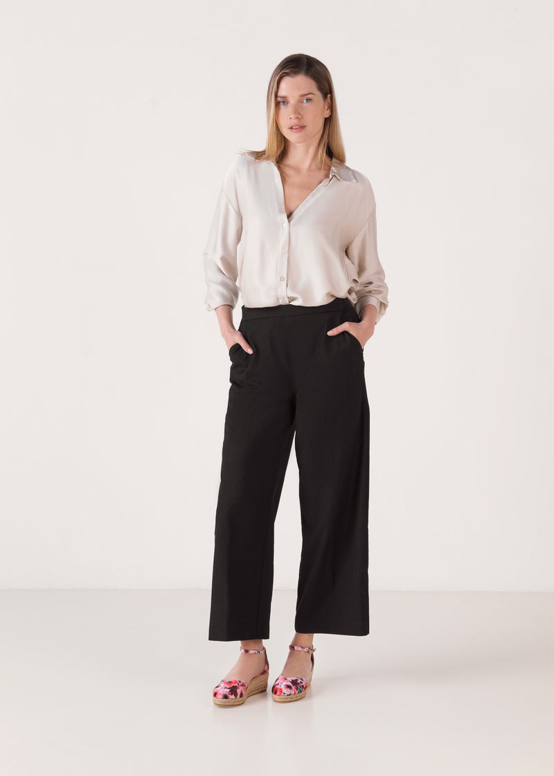 Woman wearing floral print wedge espadrilles with ankle straps, styled with a soft blouse and black cropped trousers in a clean studio setting