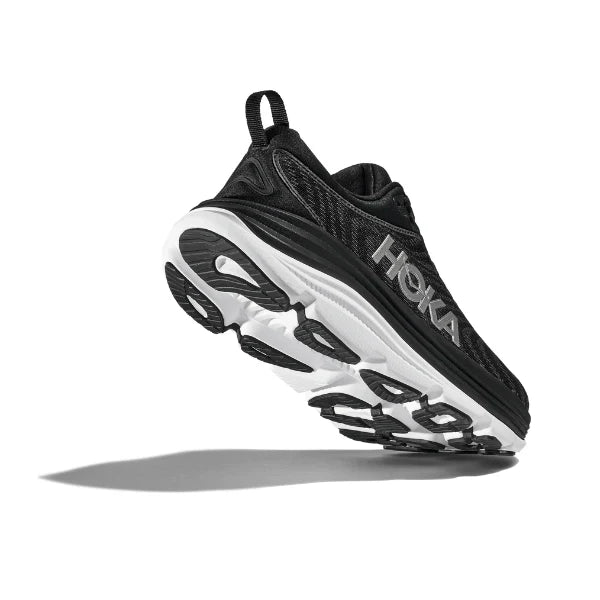 A side and slightly low-angle view of the HOKA Mens Gaviota 5 (Medium Width) in Black/White, showcasing its stabilizing H-Frame technology and visible sole, with a shadow cast on a white background.