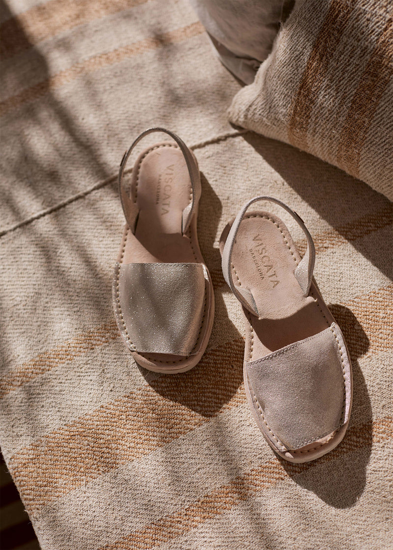 Pair of women’s metallic gold leather espadrille sandals with slingback straps and natural jute soles, styled on a sunlit woven rug.
