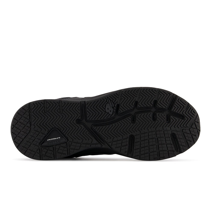 The image shows the black rubber outsole of the New Balance Mens MX857 V3 Wide Black, featuring textured patterns for grip, NDURANCE near the heel, an NB logo, and ROLLBAR technology for enhanced stability—ideal for those with foot pain.