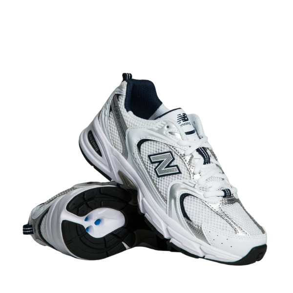 A pair of NEW BALANCE Unisex 530 White/Grey sneakers with silver and navy accents is shown—one upright, one on its side revealing the sole and side logo—designed for high mileage running and lasting comfort.