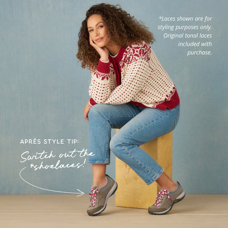 Woman sitting on a wooden block wearing a patterned sweater, jeans, and shoes with pink laces against a blue background. Copy states: "*laces shown are for styling purposes only. Original tonal laces included with purchase. Après style tip: switch out the *shoelaces!"