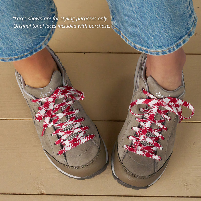 Gray sneakers with red and white checkered laces on a wooden floor. Copy states: "Laces shown are for styling purposes only. Original tonal laces included with purchase."