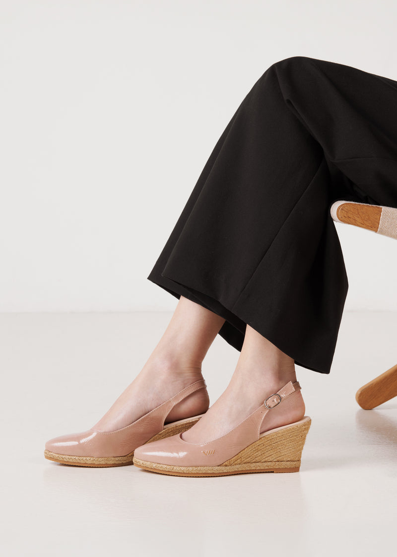 Close-up of blush pink leather wedge espadrille sandals styled under black wide-leg trousers in a clean studio setting