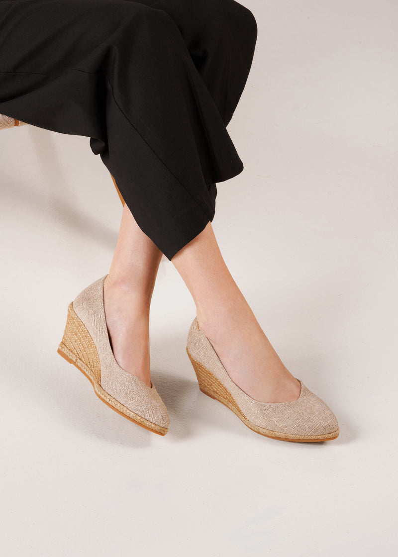 Close-up of Roses gold canvas slip-on wedge espadrilles on model with crossed legs, studio shot.