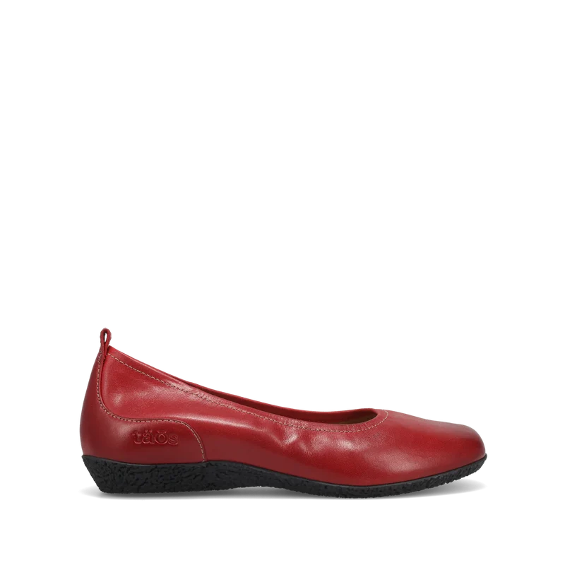 The TAOS Womens Chit Chat Red is a red leather skimmer flat with a rounded toe, black textured sole, slight wedge heel, visible stitching, orthotic-friendly design, and a pull tab at the heel for easy on/off.