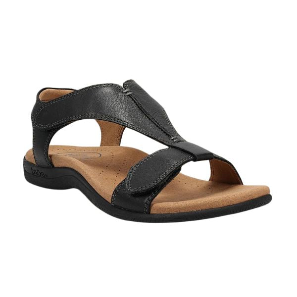 The Taos Womens The Show Black by TAOS is a black leather sandal with open toe and heel, adjustable hook-and-loop straps, and a cushioned tan antimicrobial footbed on a flat black sole.