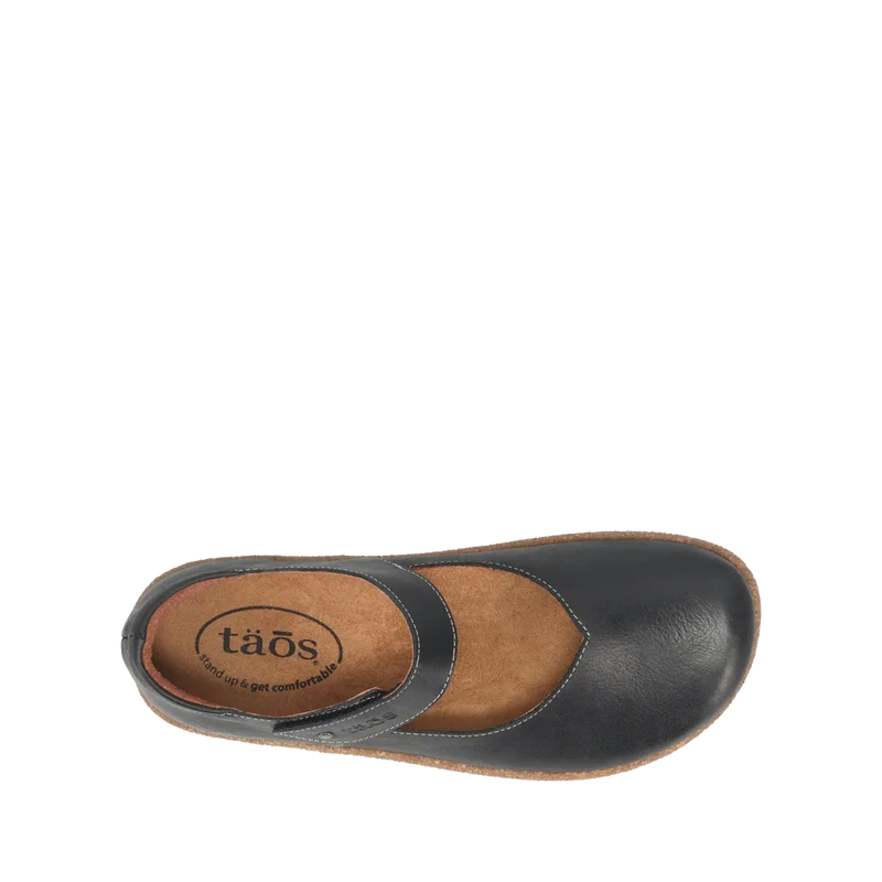 Top view of the Taos Women's Ultimate Leather Mary Jane Black shoe, featuring a black leather upper, instep strap, brown cushioned insole with arch support, and TAOS branding—ideal for women seeking comfortable footwear.
