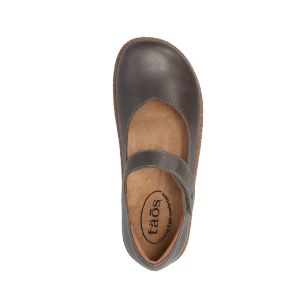 The Taos Women's Ultimate Leather Mary Jane in grey features a rounded toe, brown sole, top strap, and tan insole with TAOS branding. Designed for all-day comfort with built-in arch support.