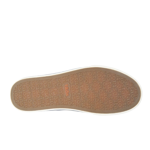 The image displays the sole of the Taos Womens Z Soul Navy/Indigo Distressed sneaker by TAOS, featuring a tan rubber texture with repeated text patterns, a central rectangular logo, and a contrasting white outer edge for style.