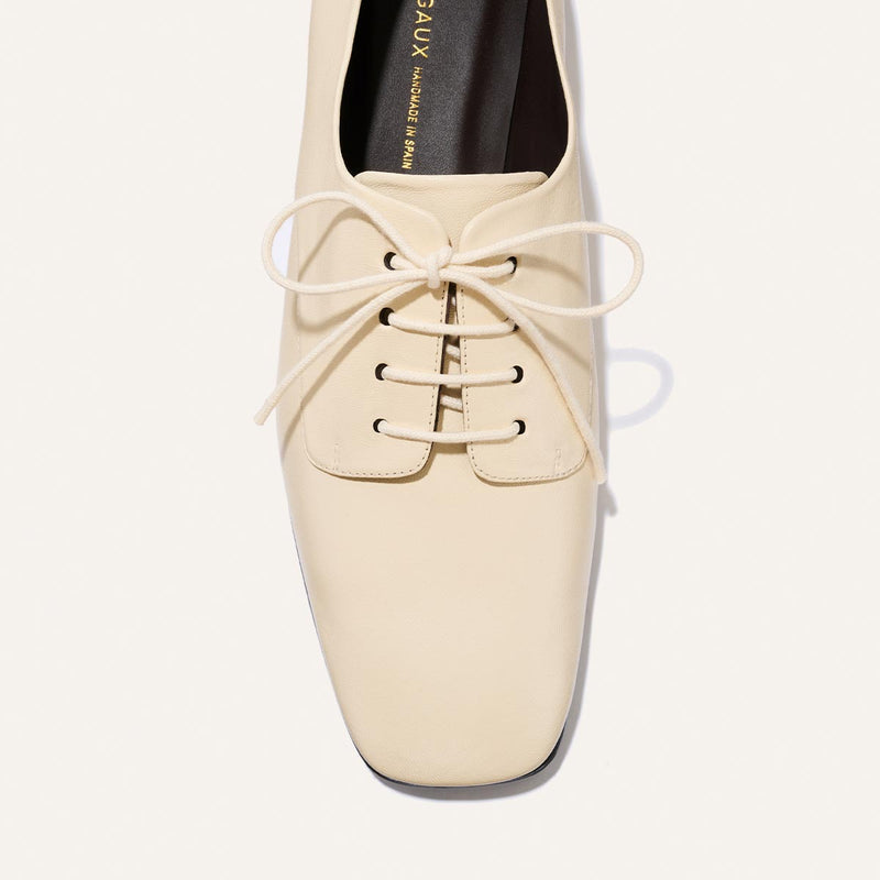 The Billie Derby - Vanilla Nappa by Margaux, a cream-colored leather lace-up oxford featuring four eyelets on each side and a neatly tied bow, is photographed from above against a white background.