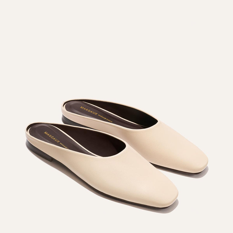 The Clara - Bone Nappa by Margaux: minimalist beige backless slip-on mules with a low heel, shown on a light background.