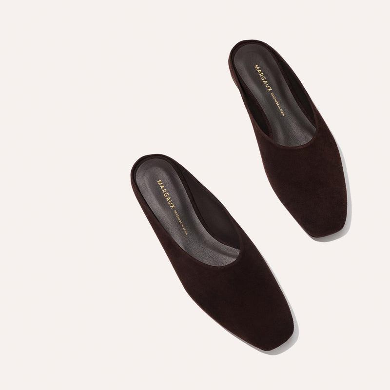 The Clara - Espresso Suede by Margaux: dark brown suede slip-on mules with a square toe and slipper-like silhouette, shown on a light beige background. Black insoles feature gold "Margaux New York" text.
