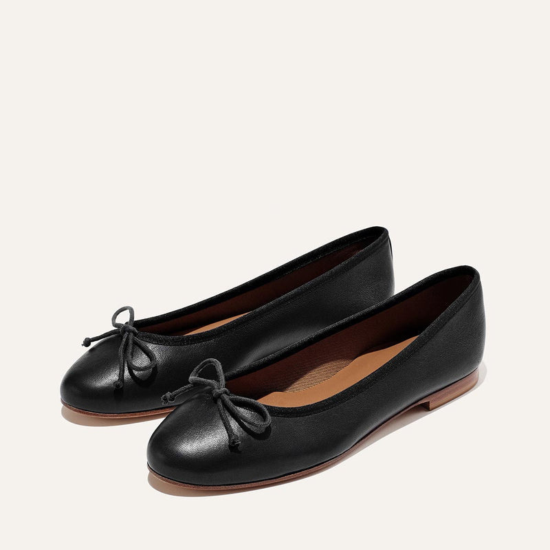 The Demi - Black Nappa by margaux-development: classic black ballet flats handmade in Spain with rounded toes, front bows, and thin brown soles, shown on a neutral background.