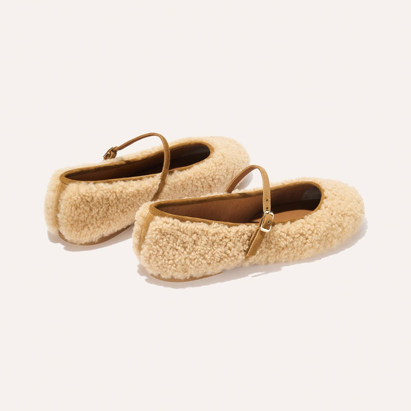 The Demi Jane - Tan Shearling flats by margaux-development feature tan fuzzy shearling texture, brown straps, and gold buckles, exuding elegant femininity against a plain light background.