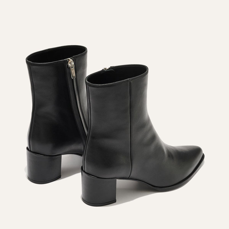 The Downtown Boot - Black Calf by Margaux is a sleek pair of black leather western ankle boots with low block heels and side zippers, shown against an off-white background.