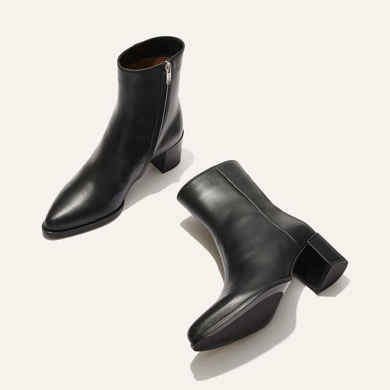A pair of black leather ankle boots with side zippers and block heels displayed on a light background, one boot upright and the other lying on its side.