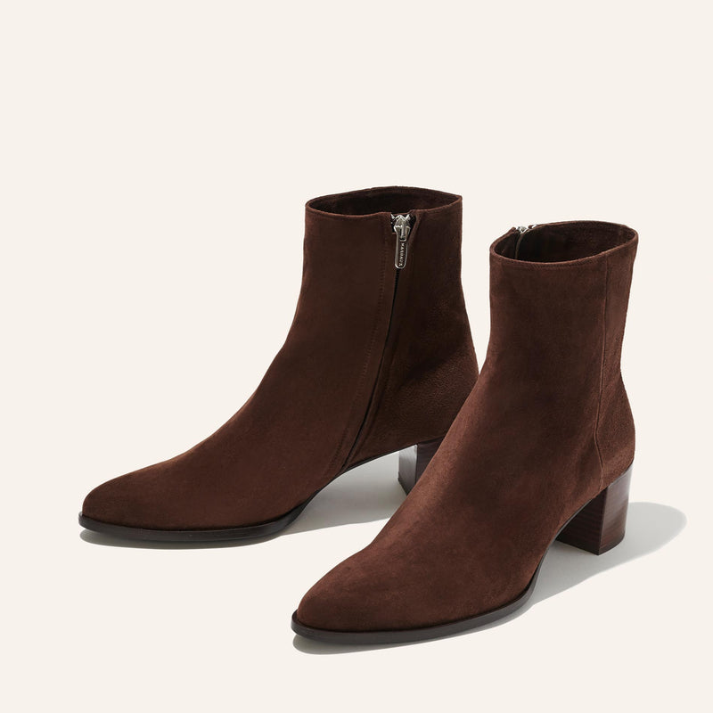 The Downtown Boot First Edition - Chocolate Suede by Margaux showcases western-inspired ankle boots with low block heels and side zippers, styled in rich brown suede and displayed against a light background.