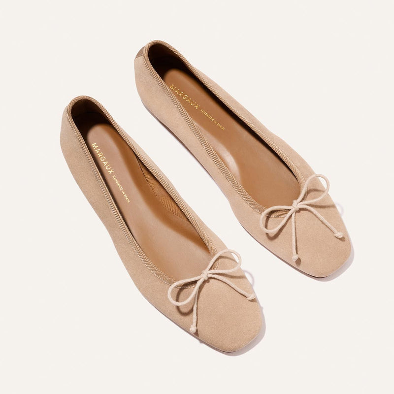 The Fonteyn - Cameo Suede by Margaux: beige suede ballet flats with square toes and decorative bows, shown on a white background.