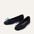 The Fonteyn - Indigo Suede by Margaux: a pair of navy blue ballet flats with small bows on the toes, displayed on a light background.