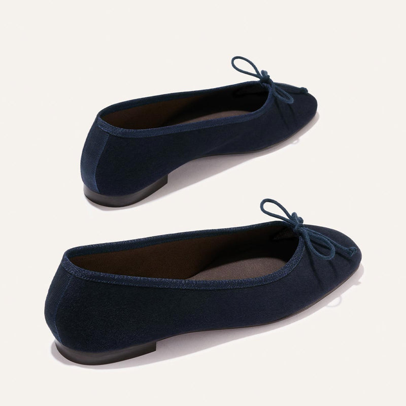 The Fonteyn - Indigo Suede by Margaux: navy blue suede ballet flats with rounded toes and small bows, shown from side and back angles on a plain light background.