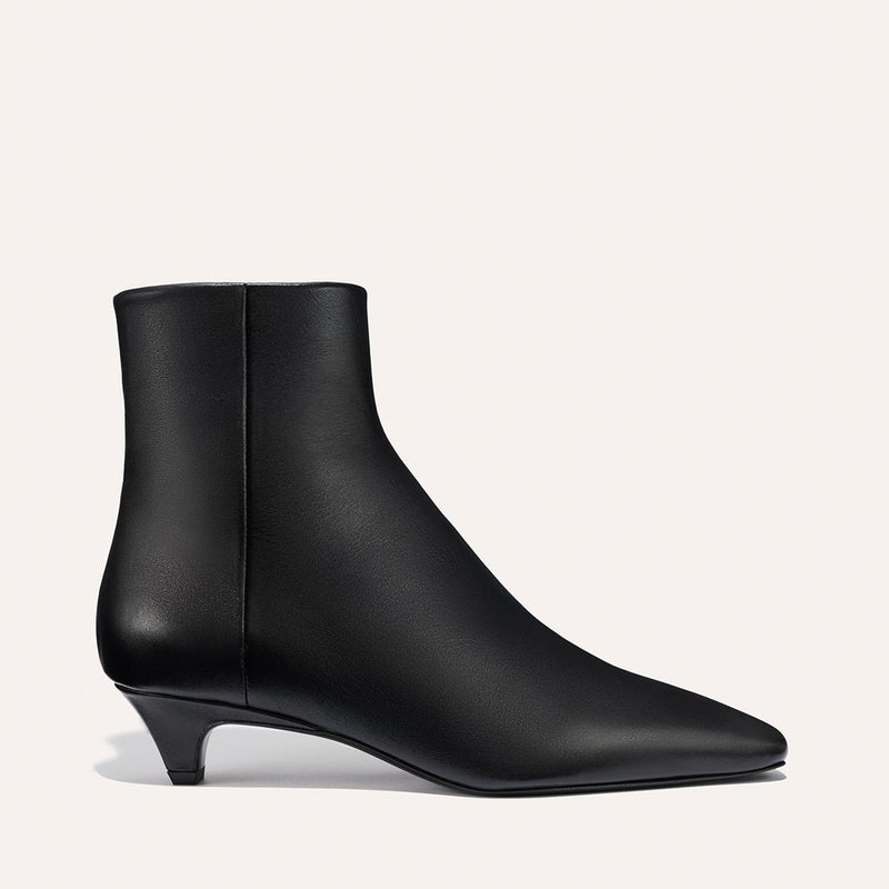 The Inga - Black Calf by margaux-development is a smooth leather black ankle boot with a low kitten heel and pointed toe, ideal for city strolls in New York, shown against a simple light background.