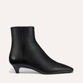 The Inga - Black Calf by margaux-development is a smooth leather black ankle boot with a low kitten heel and pointed toe, ideal for city strolls in New York, shown against a simple light background.