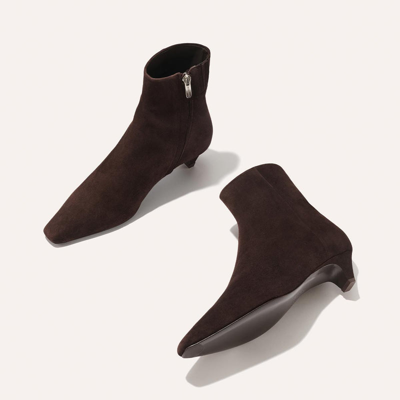 The Inga - Espresso Suede by margaux-development: dark brown suede ankle boots with pointed toes, low heels, and side zippers—ideal for NYC. One boot stands upright; the other lies on its side, revealing the sole.