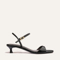 The Lotto 35 - Black Crinkle-Gloss Nappa by Margaux is a black strappy sandal with a low kitten heel, thin ankle strap with a gold buckle, and minimalist design shown against a plain light background.