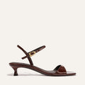 The Lotto 35 - Espresso Crinkle Patent by Margaux is a brown patent leather sandal with a low kitten heel, open toe, and slim ankle strap with a gold buckle, shown on a plain light background.