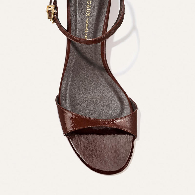 A close-up top view of Margaux's The Lotto 35 - Espresso Crinkle Patent, a brown open-toe heeled sandal with a single toe strap and an ankle strap featuring a small gold buckle.
