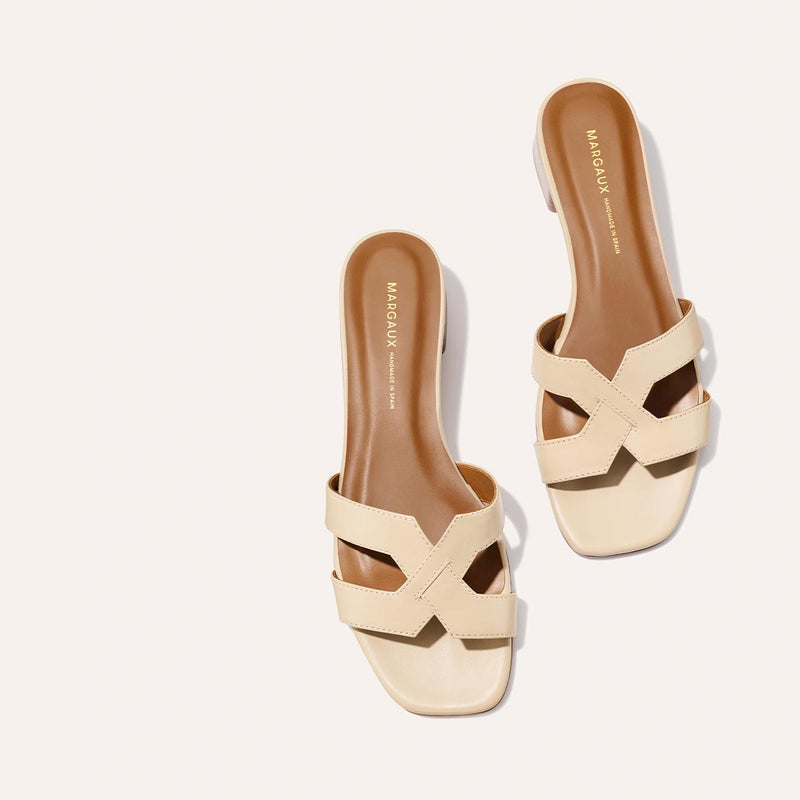 The MX 35 - Latte Calf by Margaux: beige slip-on sandals with crisscross straps, tan footbed, comfortable block heel, and square toe. MARGAUX branding on the insole; displayed on a light background.
