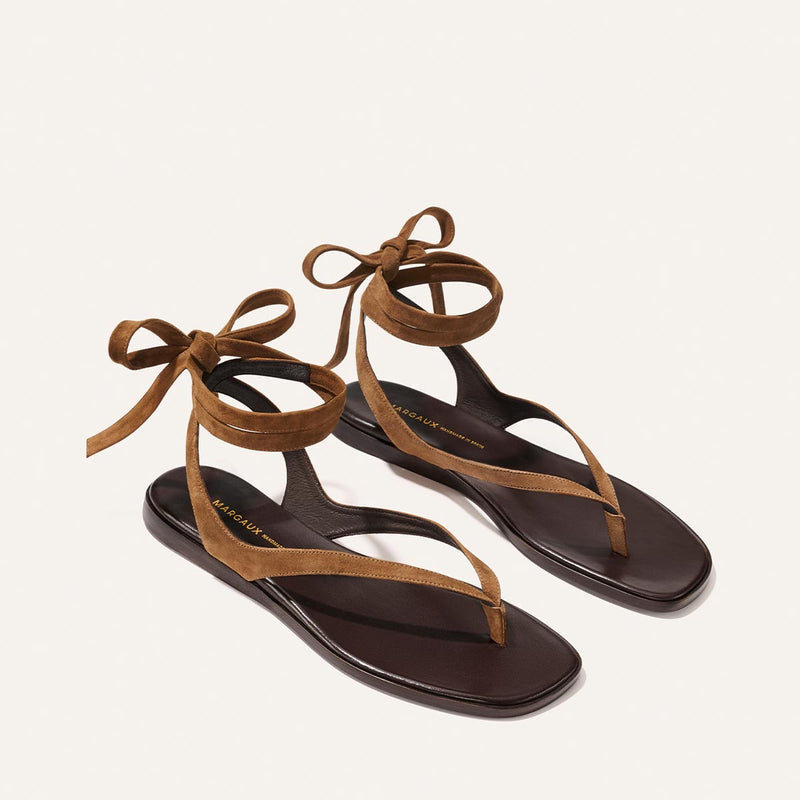 The Palermo Wrap Sandal by Margaux in Nutmeg Suede features minimalistic straps and ankle ties, crafted from suede and displayed on a light background—the perfect flat sandal for summer.