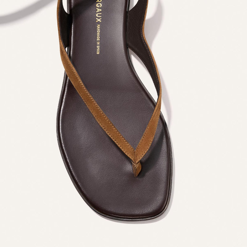 A close-up of Margaux’s The Palermo Wrap Sandal in Nutmeg Suede, featuring a brown square toe, tan suede strap, and cushioned insole—ideal for laid-back getaway style against a white background.
