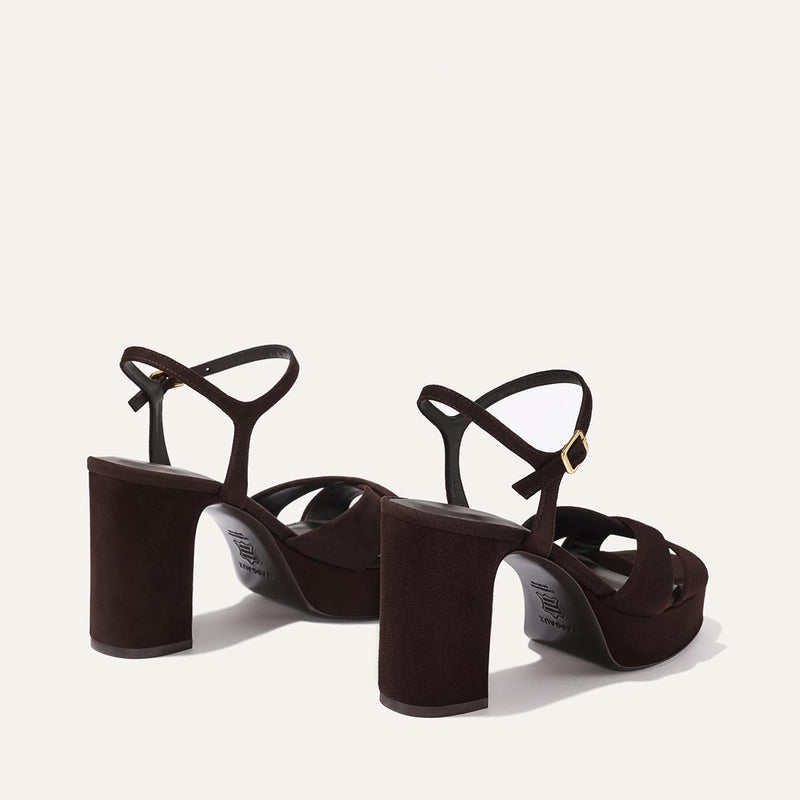 The Margaux Paloma Platform in Espresso Suede features chunky block heels, gold-buckled ankle straps, and a padded platform for comfort—all showcased on a light beige background.