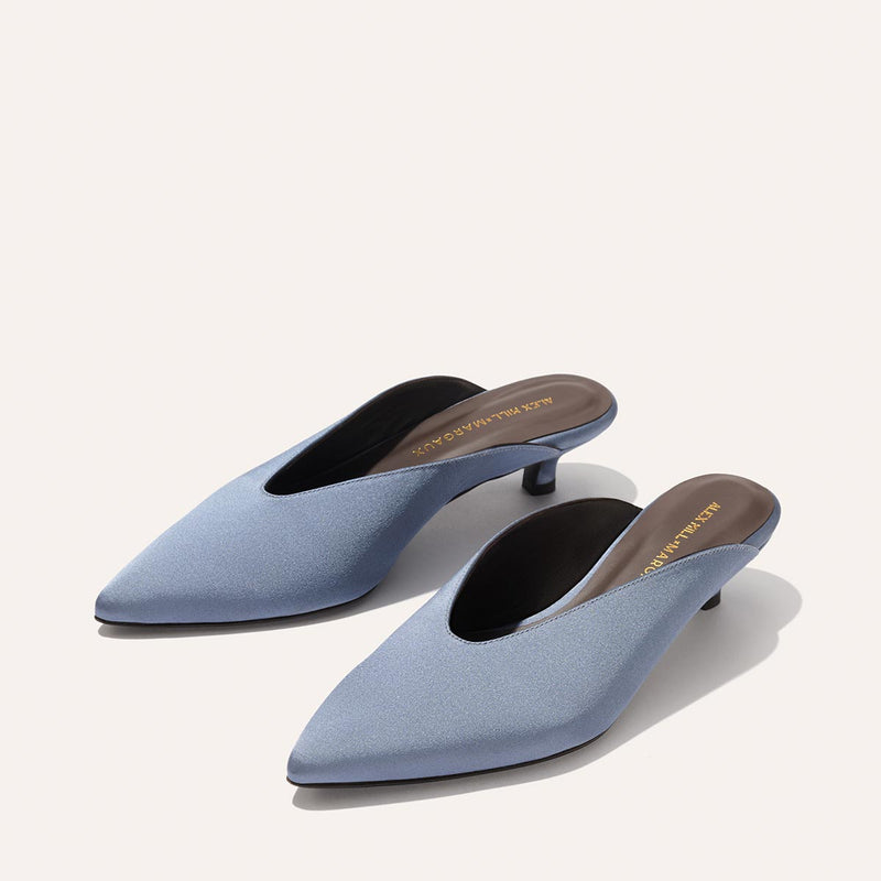 The Romy - Slate Blue Satin by Margaux are sleek, satin kitten mules with pointed toes and low, elegant heels—perfectly comfortable party shoes, shown here on a neutral background.
