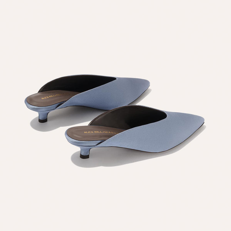 The Romy - Slate Blue Satin by Margaux features light blue, pointed-toe kitten mules with low heels and brown insoles—an elegant choice for any occasion. Displayed on a plain light background.