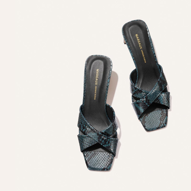 The Selene 50 - Aqua Python Embossed sandals by Margaux feature crisscross straps, a dark blue and black snakeskin pattern, square toes, and “Margaux New York” insoles, shown against a light background.