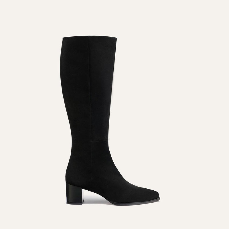 The Uptown Boot - Black Suede by margaux-development is a black knee-high boot with a block heel, crafted from suede-like material and displayed in profile against a light beige background.