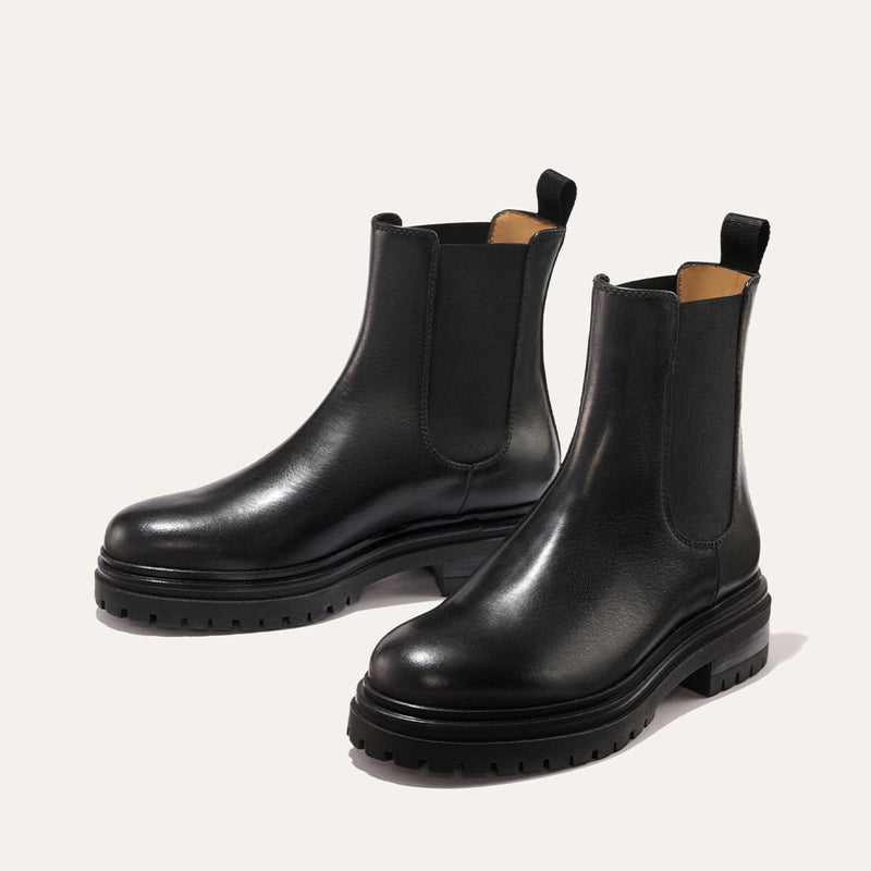 The West Chelsea Boot - Black Calf by margaux-development features chunky lug soles, elastic side panels, and back pull tabs, shown in black on a light background.