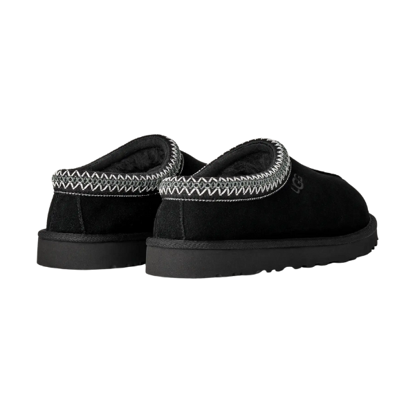 The UGG Men's Tasman II Black features a suede upper, thick black soles, and white zigzag stitching around the ankle. Shown from back and side angles, these slip-on shoes highlight UGG’s signature style.